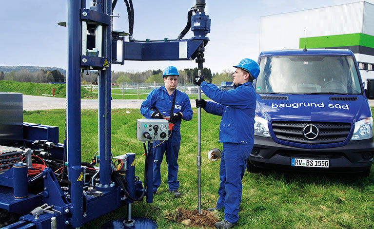 Baugrund erkunden Erkundungskonzept Zwei Personen mit Bohrgerät bei einer Baugrunderkundung auf Wiese