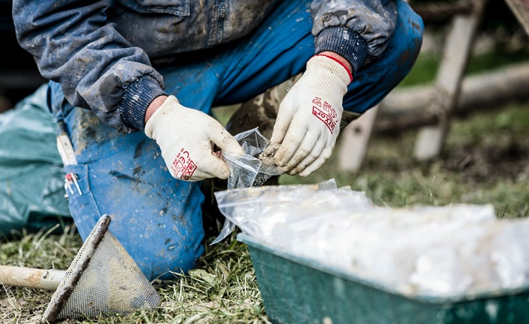 Baugrund erkunden Eine Person kniet auf dem Boden bei Untersuchung des Baugrunds